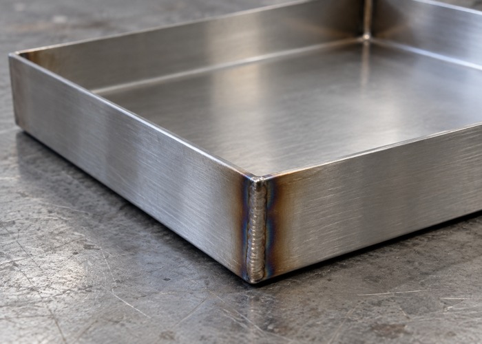 Welded stainless tray corner with localized heat tint before finishing