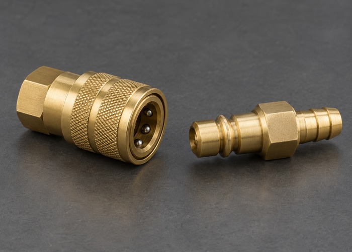 Separate brass quick coupling socket and plug on a gray bench
