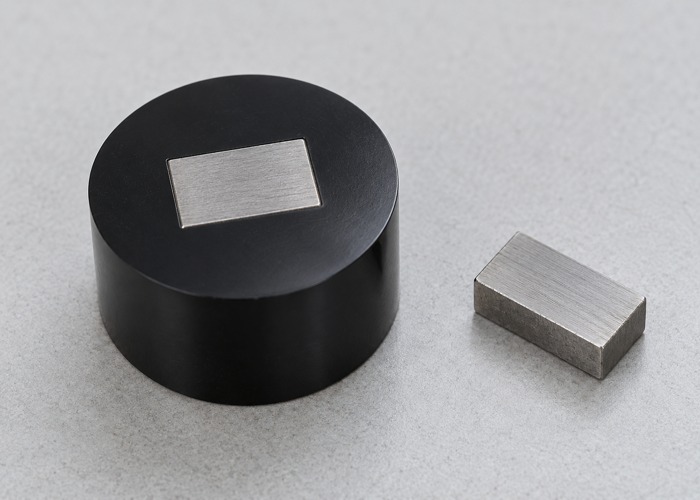 Rectangular steel specimen in a black resin mount beside a steel offcut