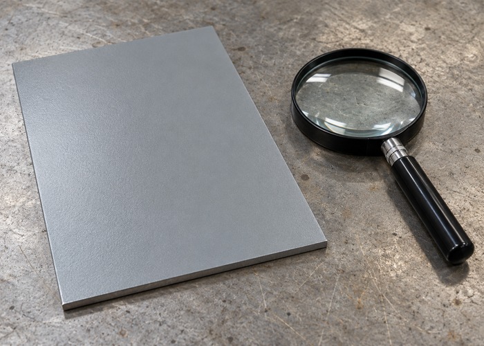 Gray coated sample panel beside a handheld magnifying glass