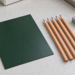 Green coated metal coupon beside wooden pencils and a sharpener